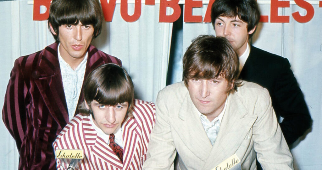 Die vier Mitglieder der Beatles bei einer Pressekonferenz vor mehreren Mikrofonen.